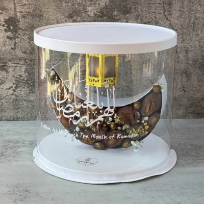 Luxury Ramadan gift box featuring a crescent moon filled with chocolate-covered dates and assorted nuts, elegantly presented in a clear round box with a lantern