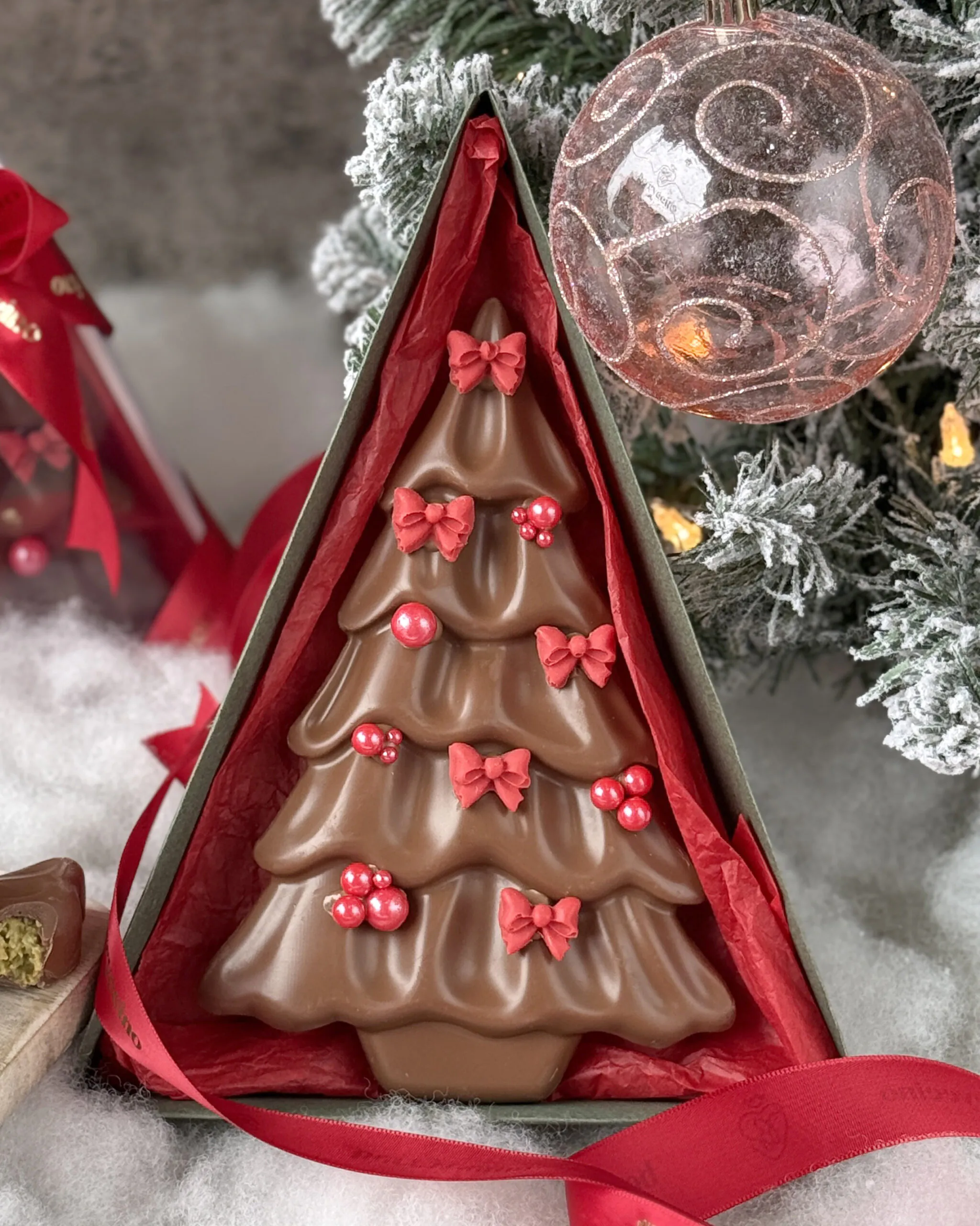 Close-up of Christmas Tree Chocolate – Dubai Edition with red bows and pearls in a luxury triangle box.